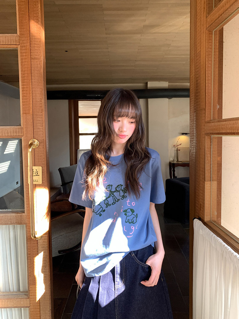 Young woman wearing a blue graphic T-shirt and denim skirt indoors