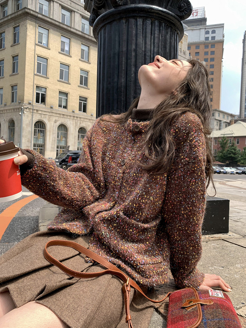 Model wearing a speckled brown knit cardigan and carrying a plaid handbag outdoors