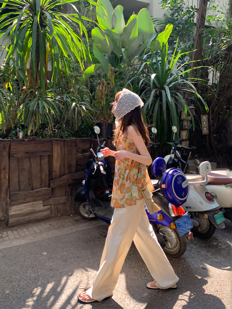 Woman wearing an orange floral sleeveless top with cream wide-leg pants in a tropical outdoor setting