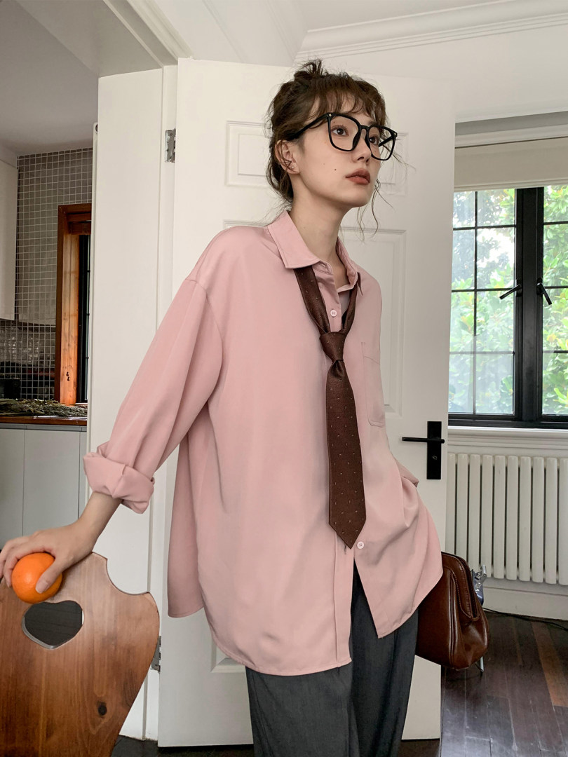 Model wearing a loose pink button-up shirt with a brown tie and glasses