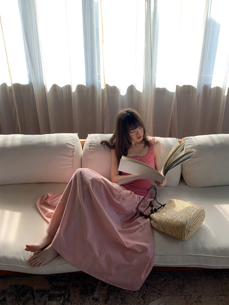 Woman wearing a pink sleeveless dress or matching set while sitting on a couch reading