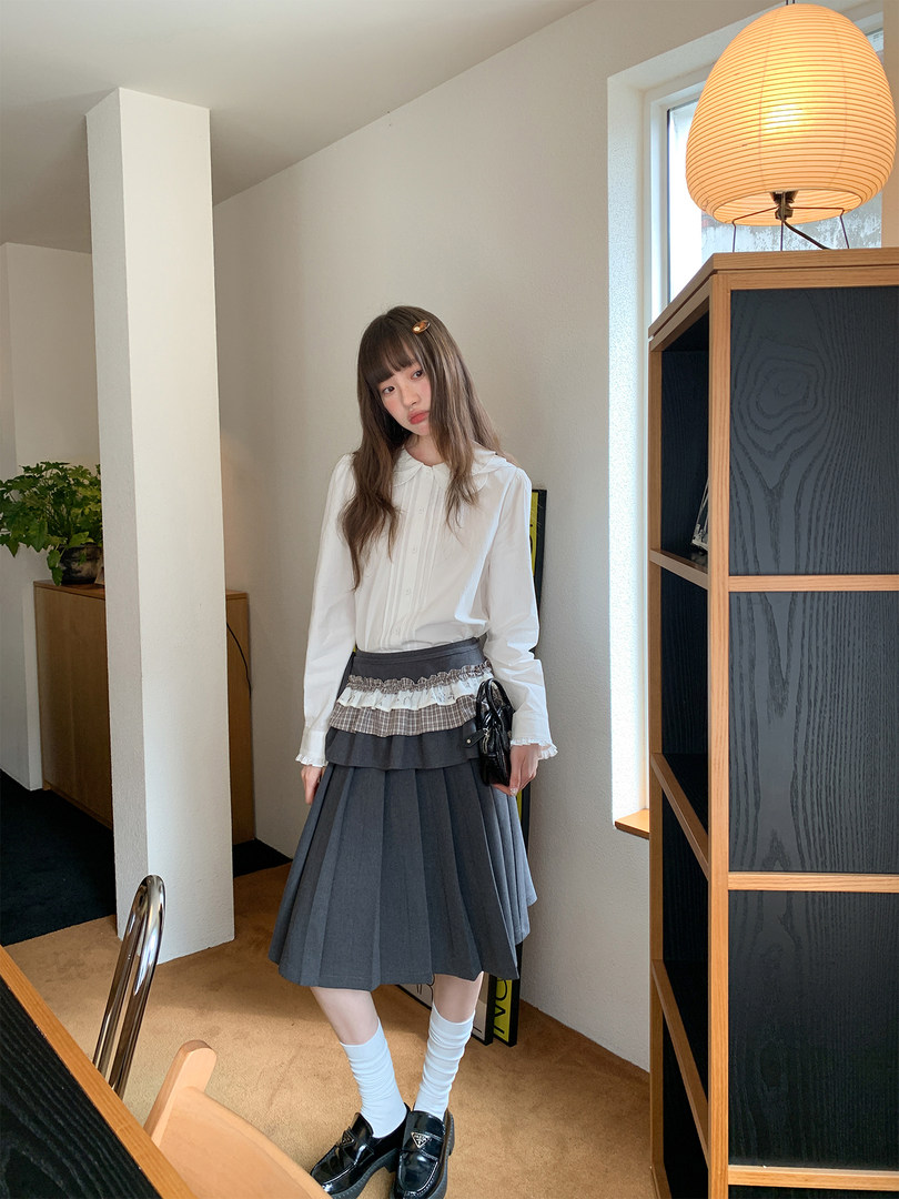 Model wearing a white blouse with a gray pleated skirt and loafers