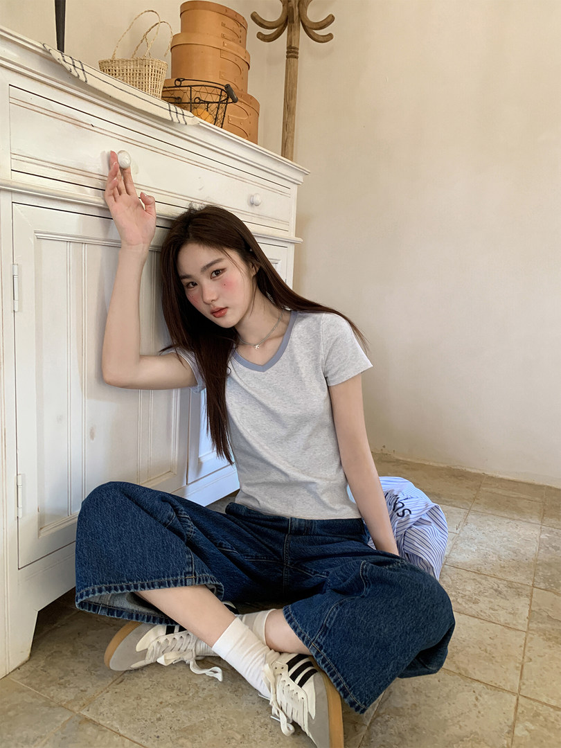 Model wearing a light gray V-neck T-shirt with dark wide-leg jeans and sneakers