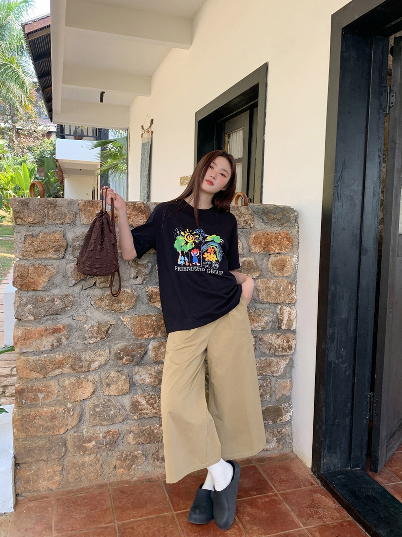 Woman modeling a black graphic T-shirt with beige wide-leg pants and black shoes