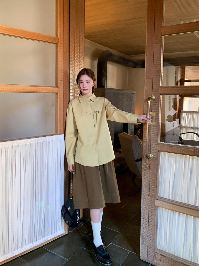 Woman wearing a pale yellow button-up shirt and brown skirt outfit