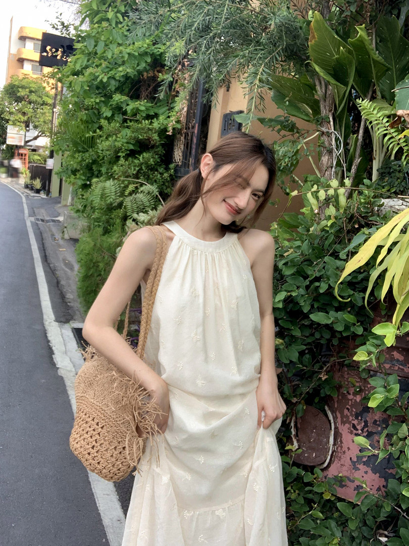 Cream sleeveless dress worn by a model with a woven straw bag outdoors
