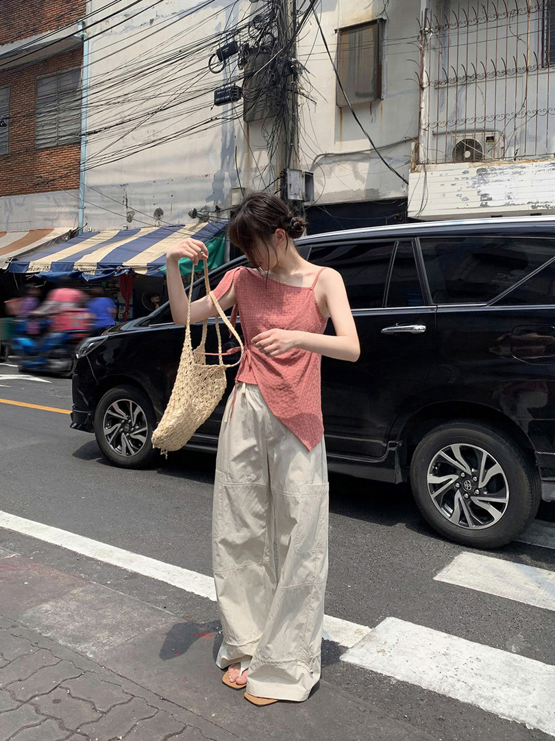 Woman wearing a pink sleeveless top with beige wide-leg pants and a woven tote bag on a city street