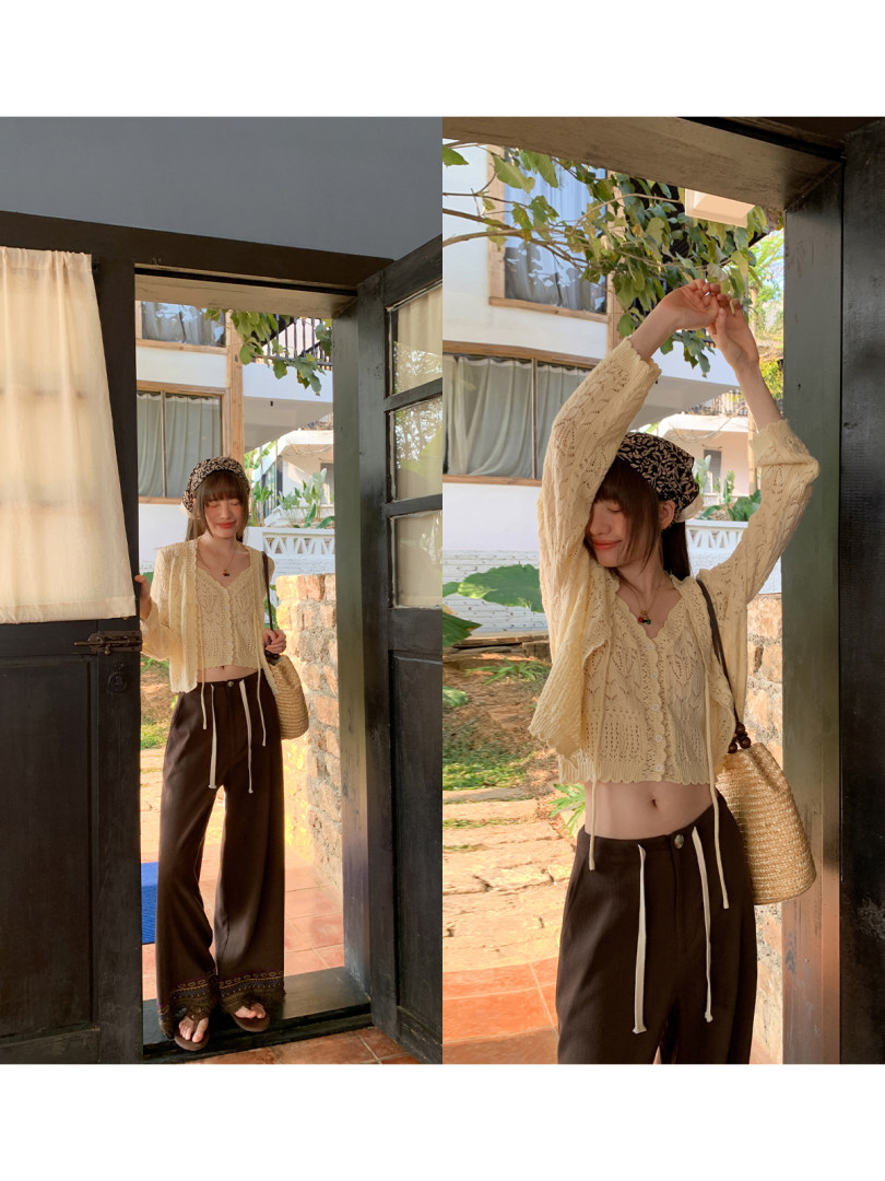 Model wearing a cream knit cropped cardigan with dark wide-leg pants and a woven bag outdoors