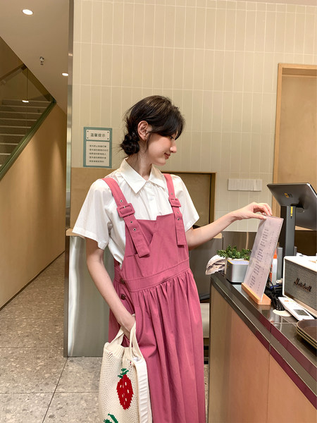 Woman wearing a pink pinafore dress over a white collared shirt
