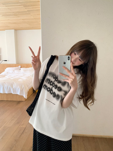 Person taking a mirror selfie wearing an oversized white graphic T-shirt and black polka dot skirt