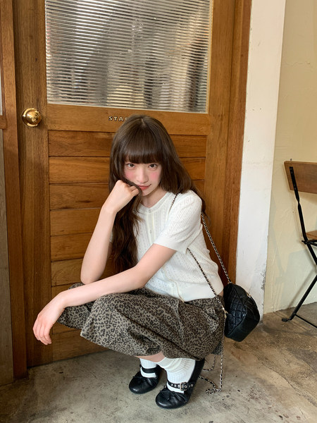Model wearing a white knit top, leopard skirt, black flats, and a small chain bag
