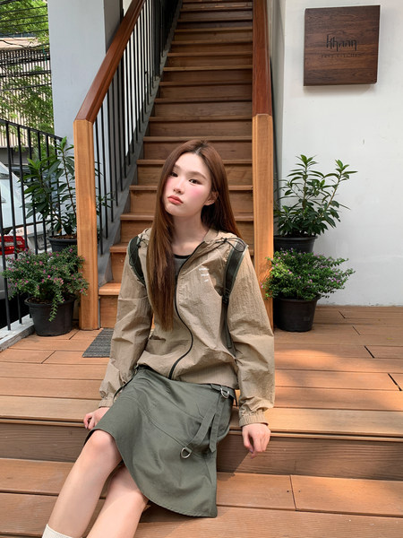 Model wearing a beige lightweight jacket and olive skirt outdoors