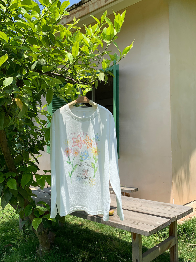 White long-sleeve graphic shirt with colorful floral print hanging outdoors