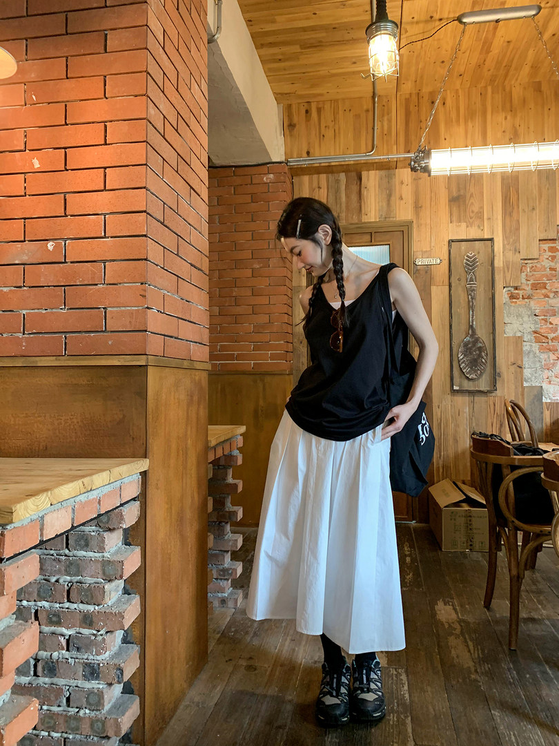 Woman wearing a black sleeveless top with a white midi skirt and black shoes