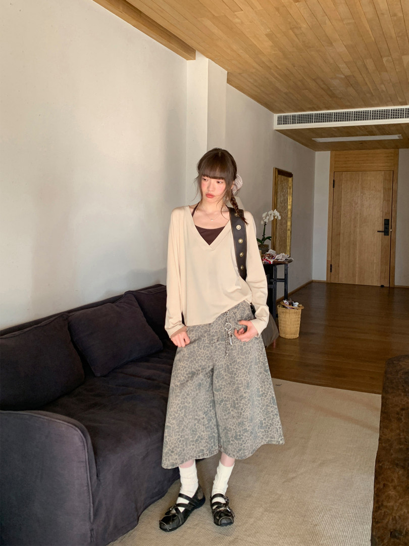 Woman wearing a cream V-neck top with patterned wide-leg pants and black sandals