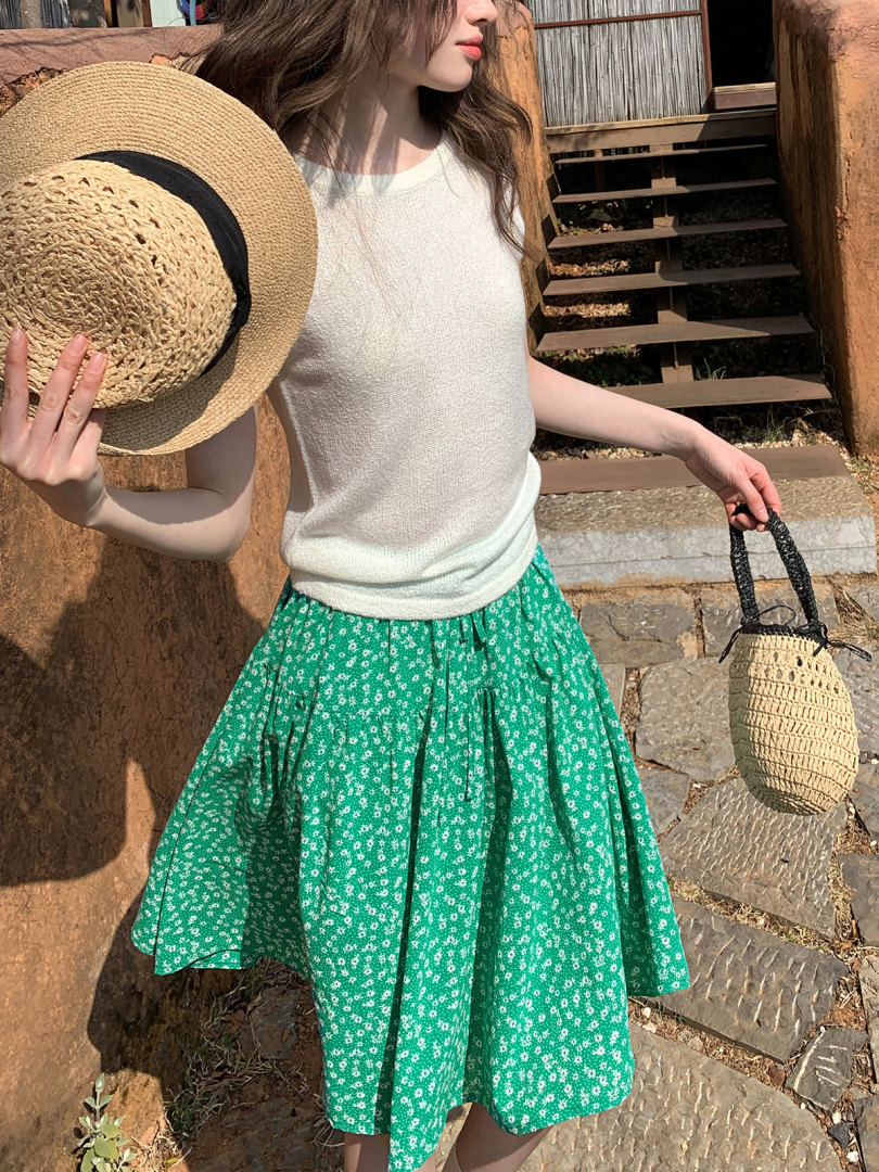 Woman modeling a white sleeveless top with a green floral skirt and straw accessories outdoors