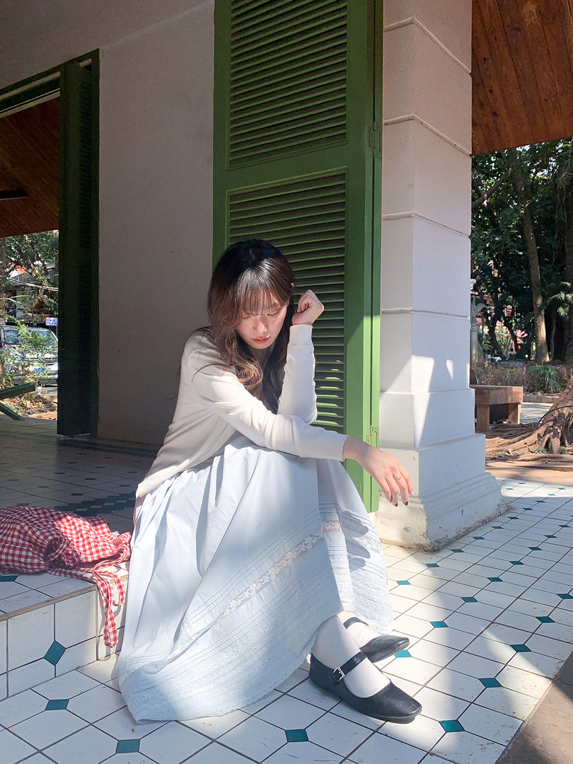 Woman wearing a white long skirt and light long-sleeve top with black shoes outdoors