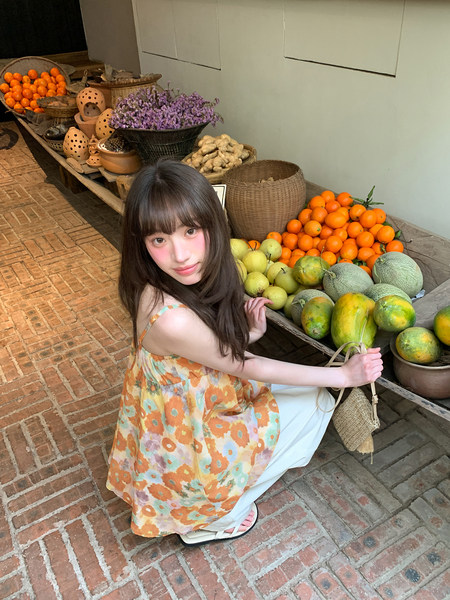 Woman wearing a colorful floral dress and white pants at a fruit market