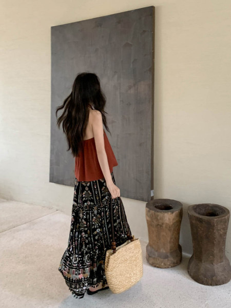 Woman wearing a rust sleeveless top with a patterned maxi skirt and woven straw bag