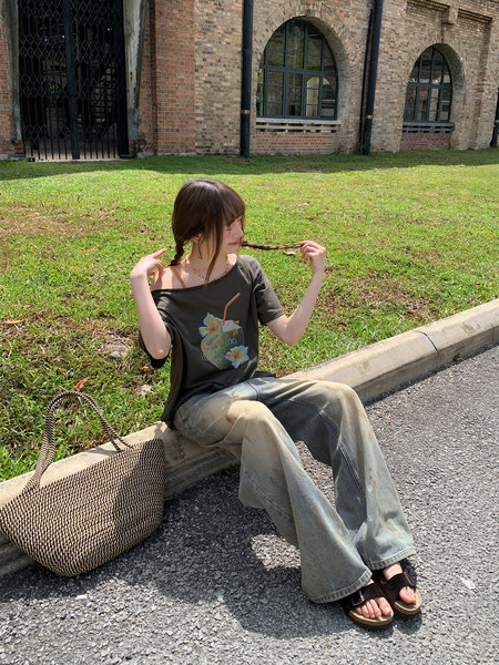Woman wearing a graphic off-shoulder tee, wide-leg jeans, sandals, and a woven tote bag outdoors
