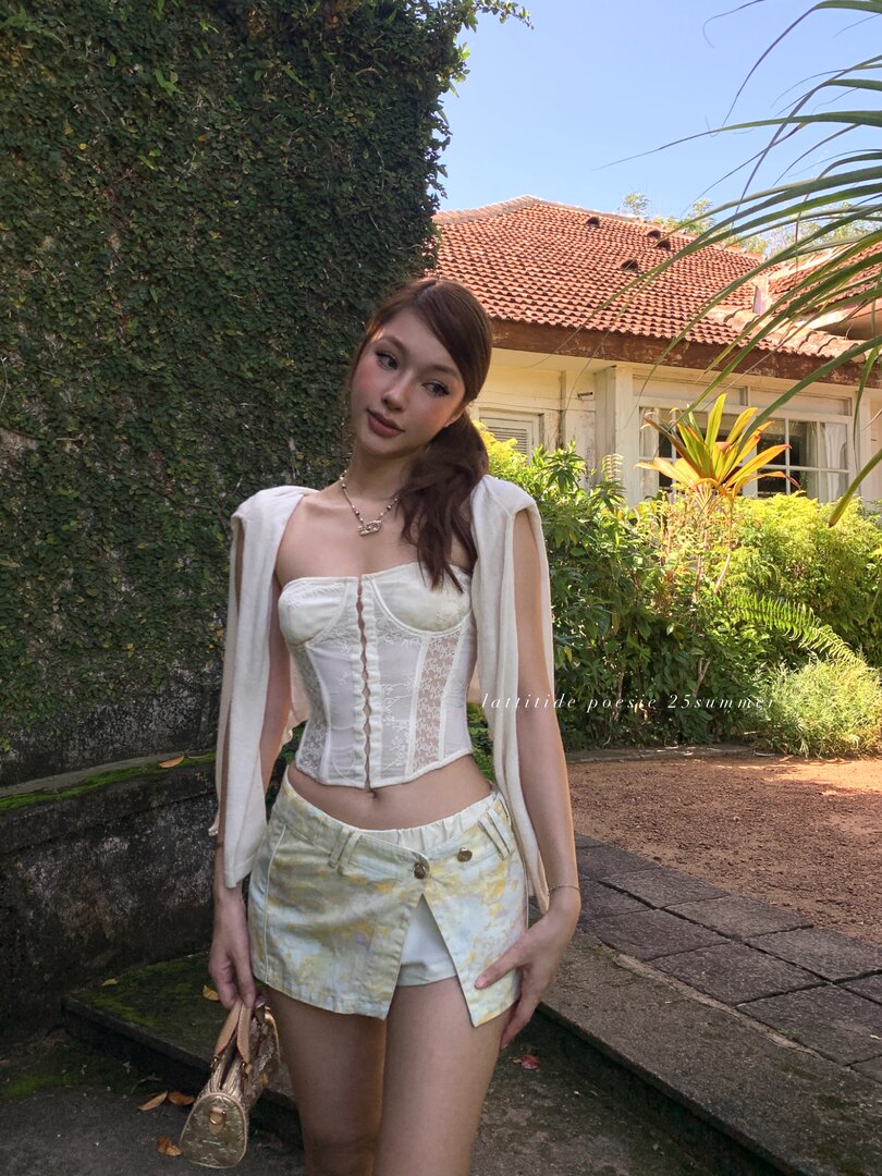 Woman wearing a white lace corset top with a light patterned mini skirt outdoors