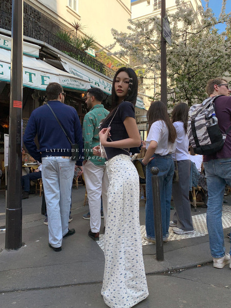 Woman wearing a black top and white floral wide-leg pants on a Paris street