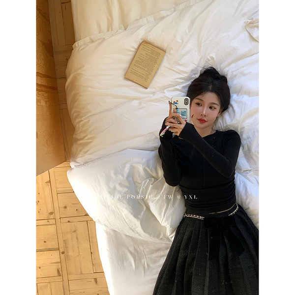 Black long-sleeve outfit worn by a model lying on a bed