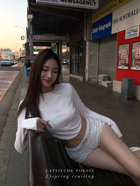 Woman wearing a white long-sleeve top and silver sequined shorts sitting outdoors