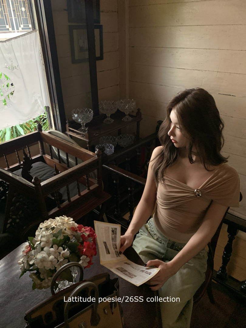 Woman wearing a draped beige off-shoulder top and light green pants indoors