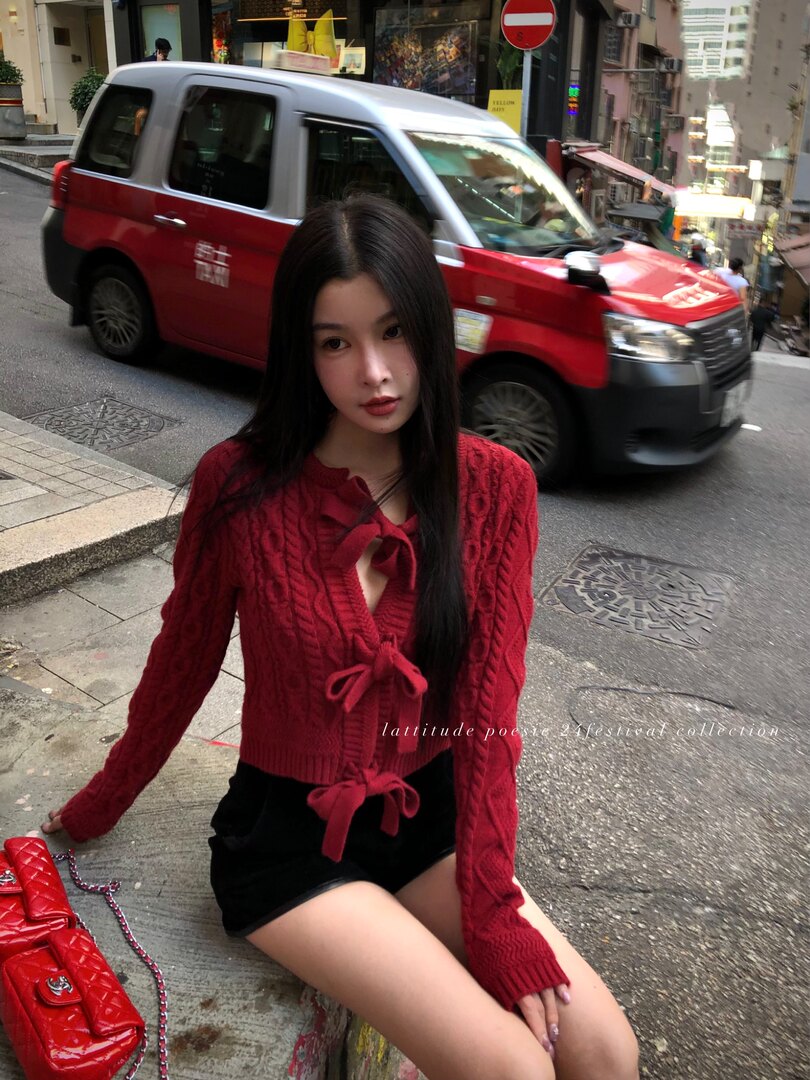Model wearing a red knit cardigan with ribbon ties and black shorts on a city street
