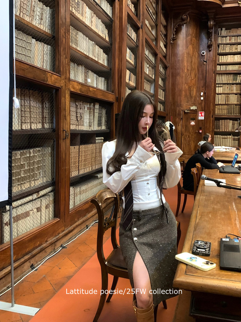 Woman wearing a white long-sleeve top and dark textured skirt in a library setting