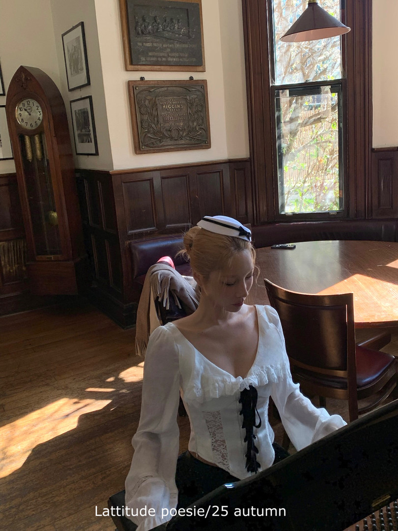 Woman wearing a white vintage-style blouse with black ribbon detail indoors