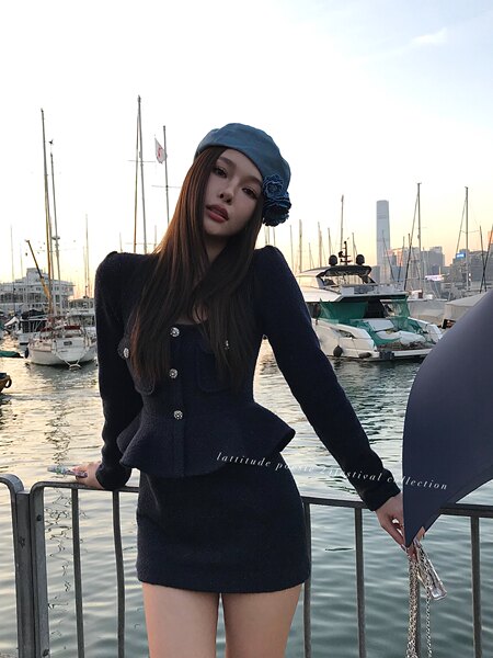 Black textured long-sleeve mini dress worn with a blue beret by a model at a marina.