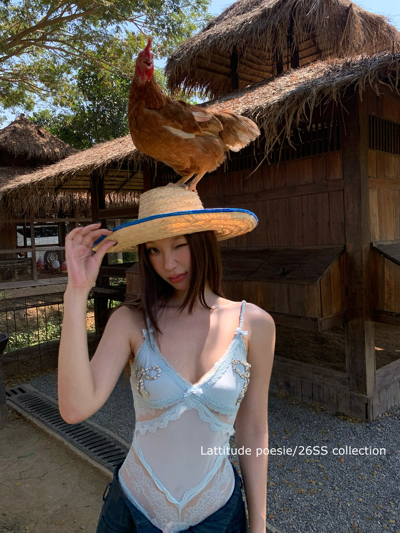 Woman wearing a light blue sheer lace bodysuit with a straw hat and chicken on top