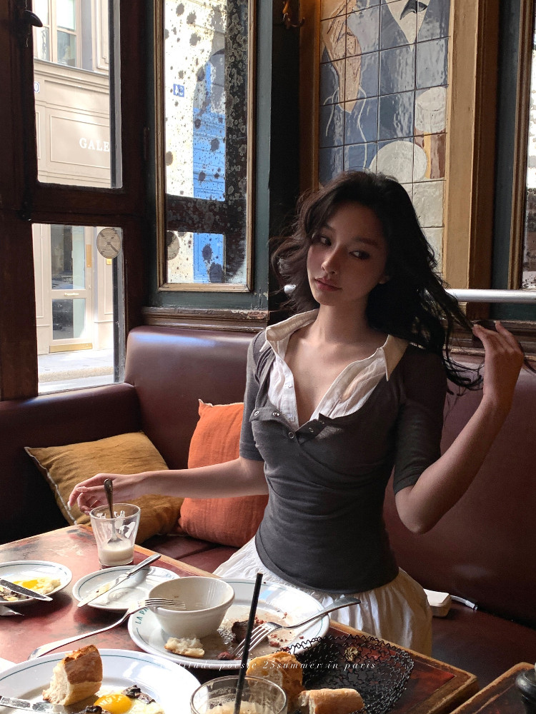 Woman wearing a fitted gray-and-white layered top seated at a cafe table