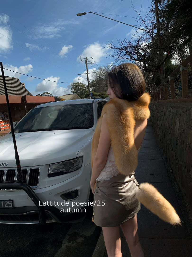Woman wearing a tan fur stole and lace-trim outfit outdoors beside a white SUV
