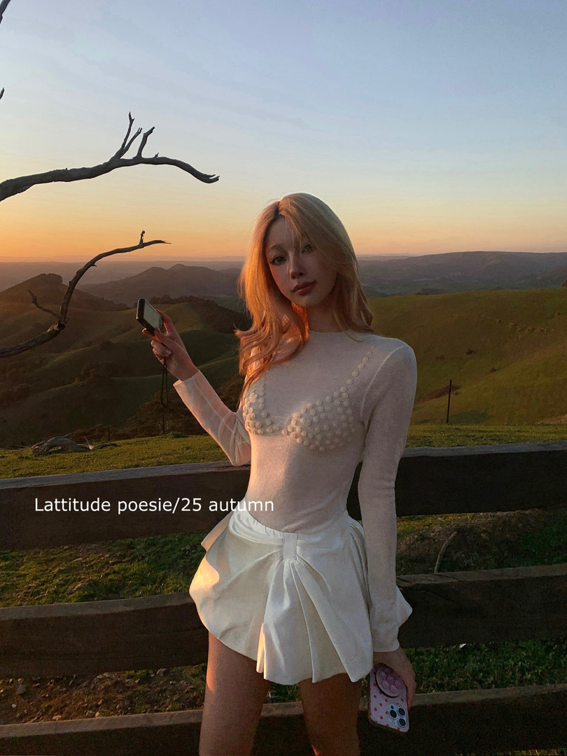 Woman wearing a white long-sleeve embellished top and draped shorts at sunset