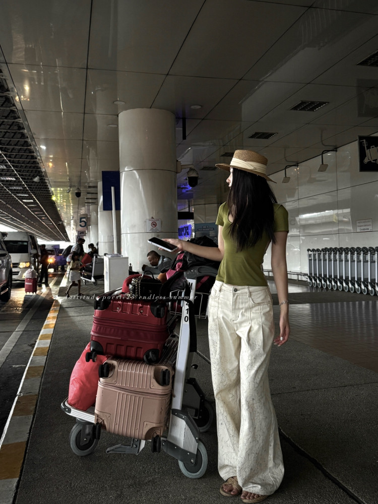 Woman wearing an olive green top and white wide-leg pants with a straw hat at an airport