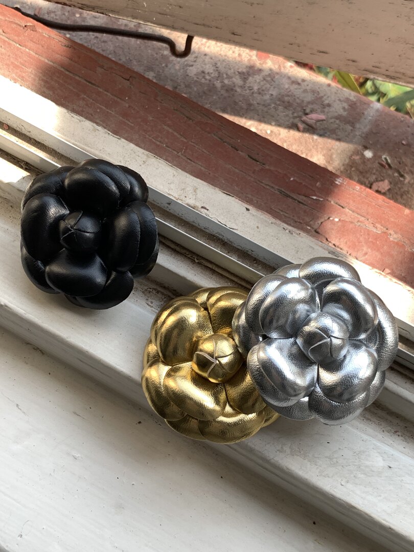 Three metallic flower-shaped decorative accessories in black, gold, and silver on a windowsill