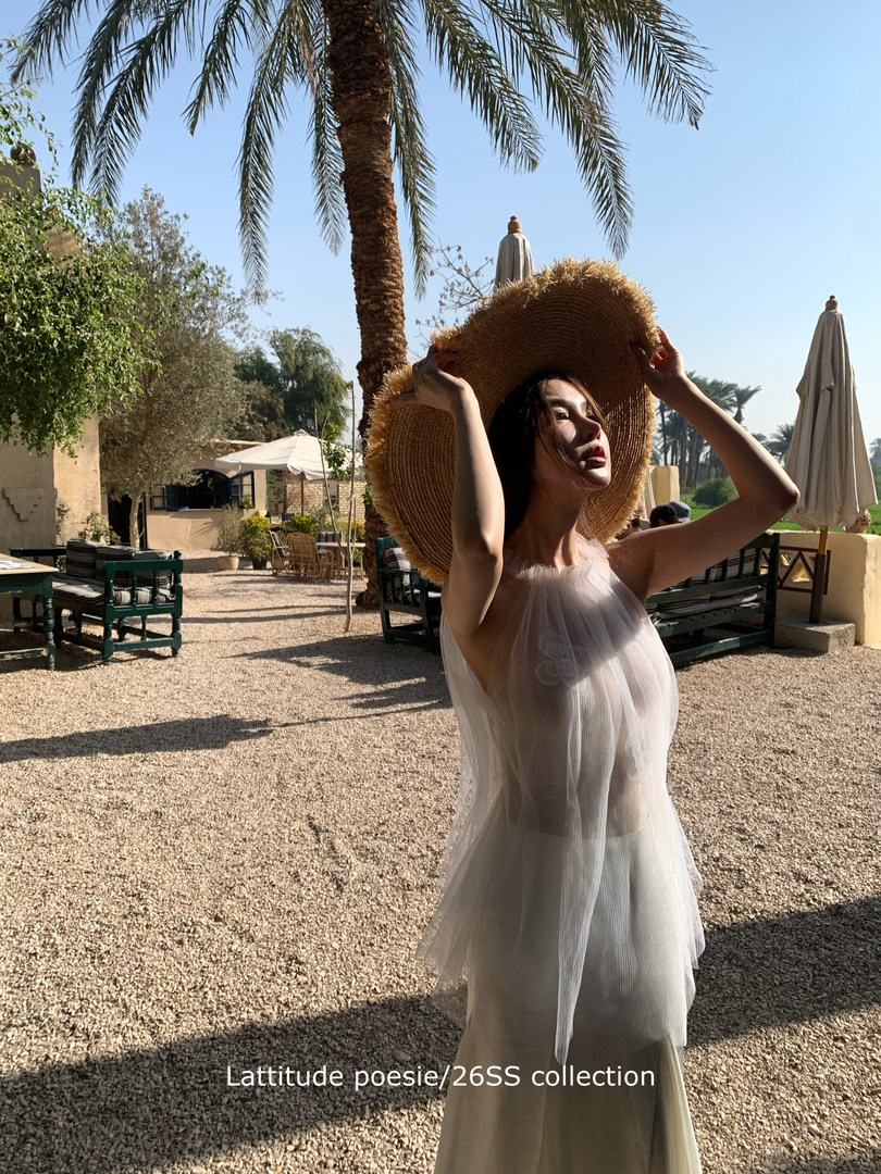 Woman wearing a sheer white resort dress and oversized straw hat outdoors