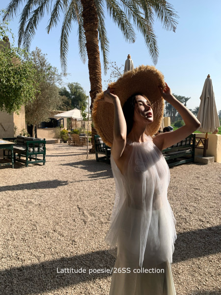 Woman wearing a sheer white resort dress and oversized straw hat outdoors