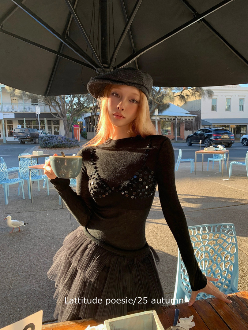 Model wearing a black embellished top, cap, and tulle skirt outdoors at a cafe