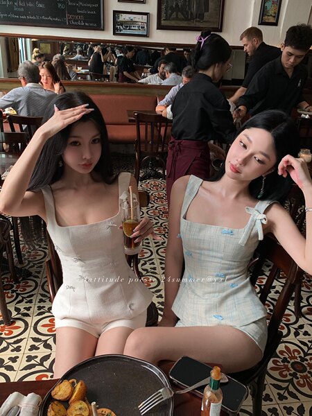 Two women wearing light summer sleeveless romper outfits seated in a restaurant