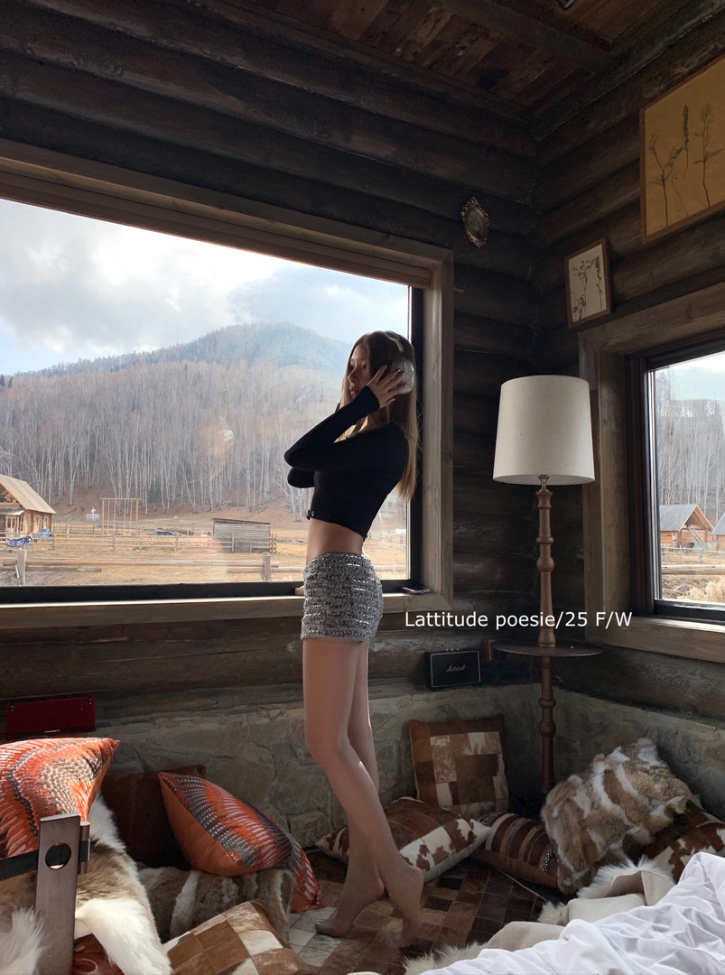Woman wearing a black long-sleeve crop top and silver sequin shorts in a rustic cabin