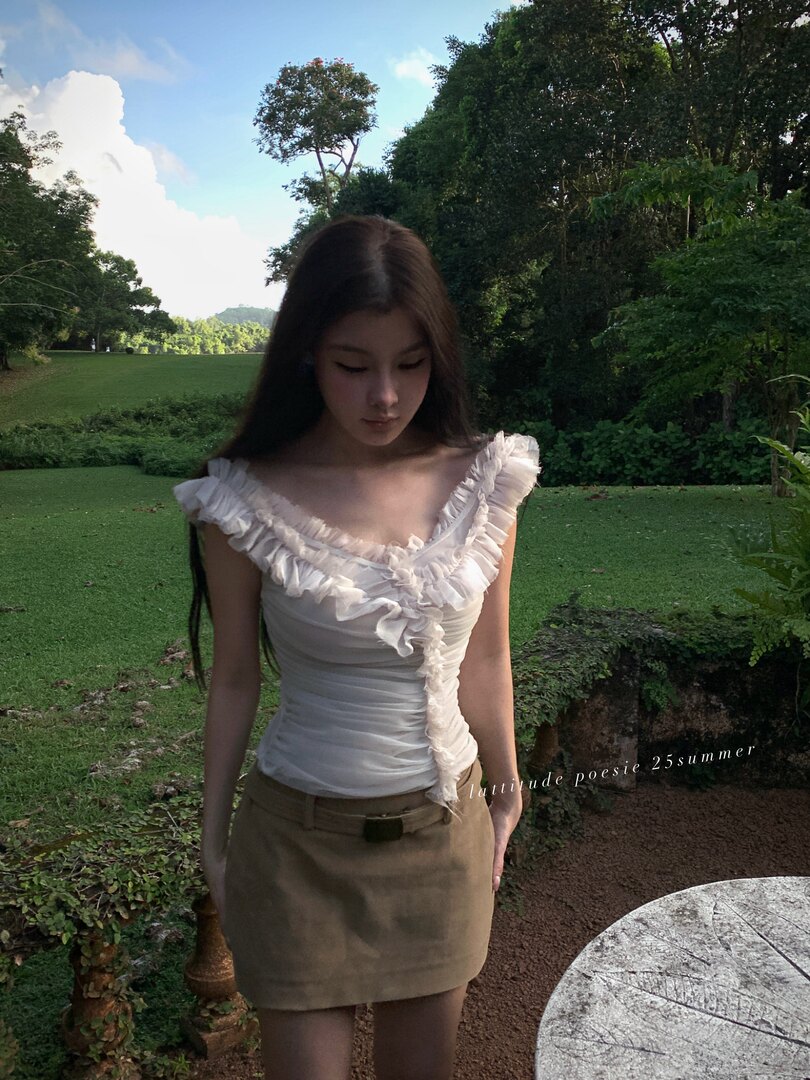 Woman wearing a white ruffled off-shoulder top and brown mini skirt outdoors