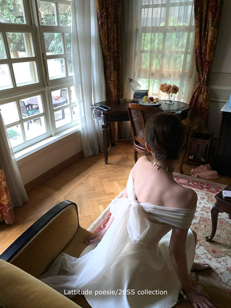 White off-shoulder dress worn by a model indoors with a flowing back bow
