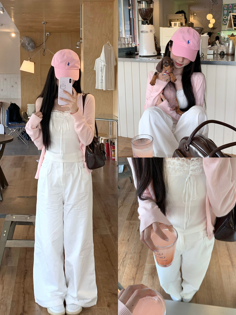 Woman wearing a pink cardigan, white lace top, wide-leg white pants, and a pink baseball cap in a cafe