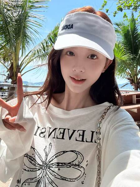 Woman wearing a white visor cap and oversized graphic T-shirt at a tropical beach setting