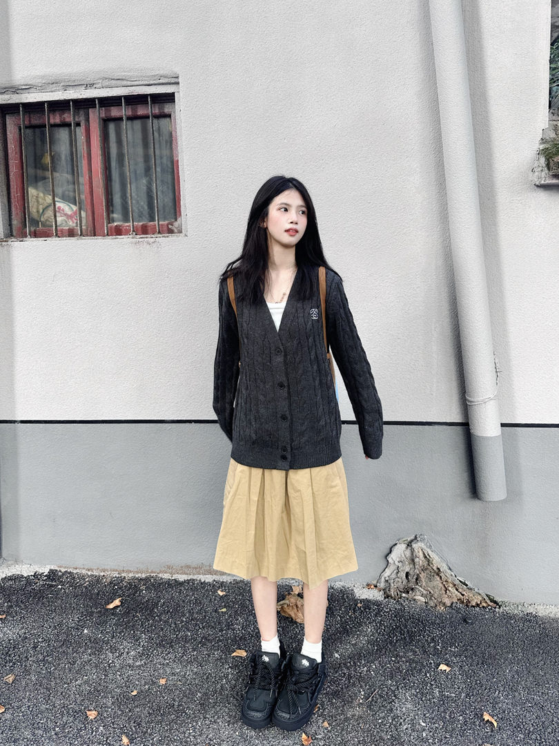 Woman wearing a dark cardigan with a beige skirt and black sneakers outdoors