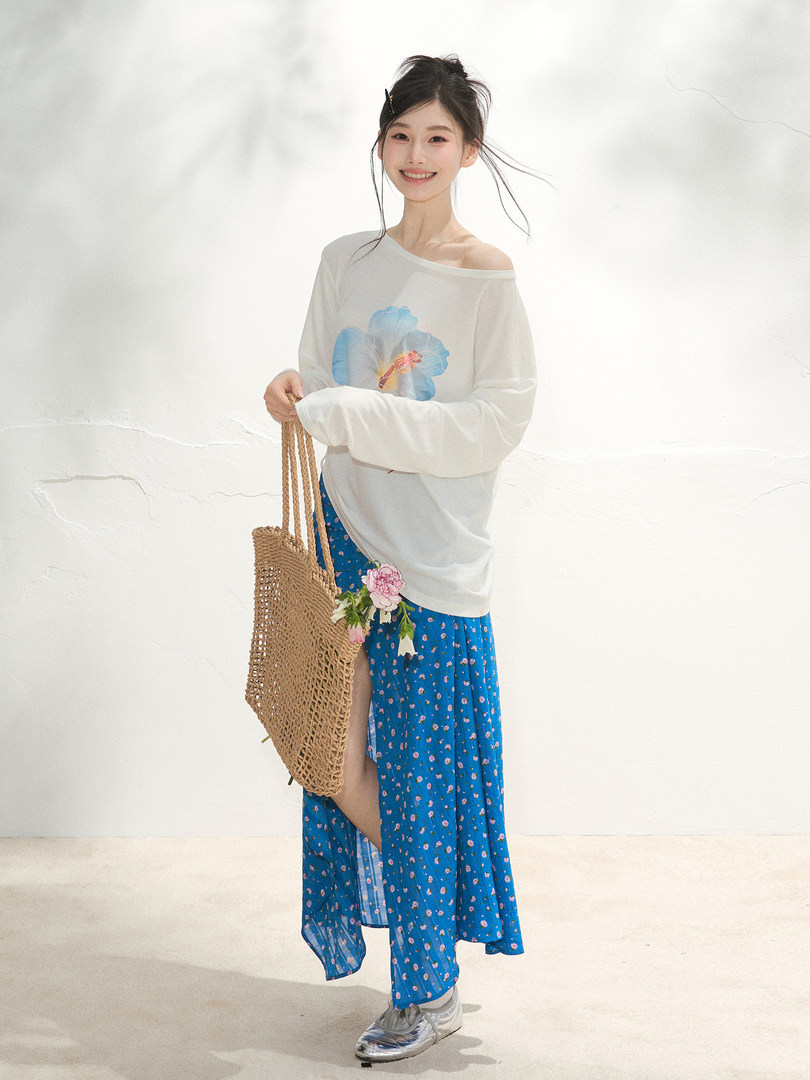 Model wearing a white floral off-shoulder top with a blue patterned skirt and woven tote bag